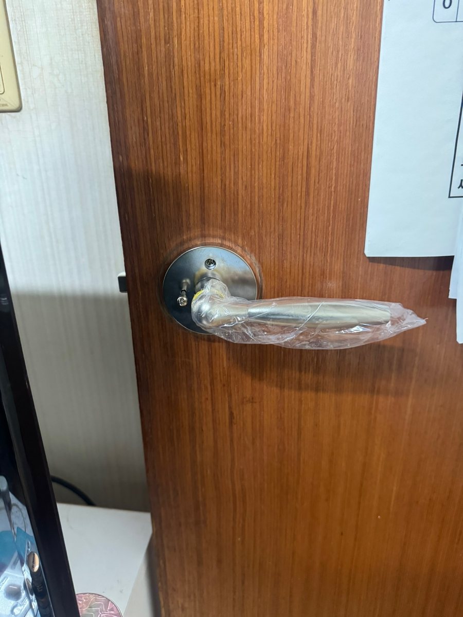 광명시 광명7동 출장 — 갈색 나무 문에 단 은색 레버 손잡이와 아직 씌워진 포장 비닐, 받침판 나사